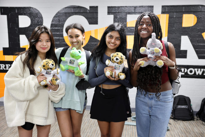 Four young women hold stuffed animals while standing in front of a Mercer mural
