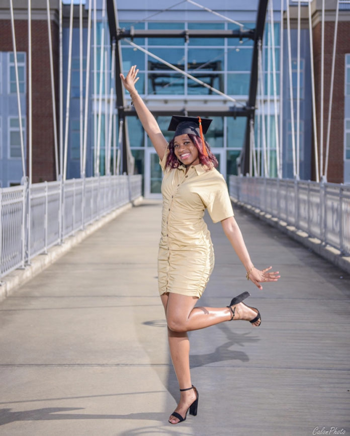 A young woman wearing a graduation cap poses on a bridge