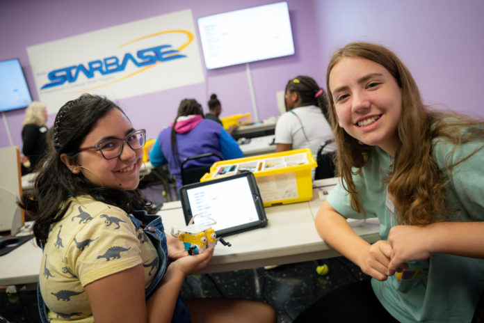Two middle school girls smile while one holds a robot made out of legos.