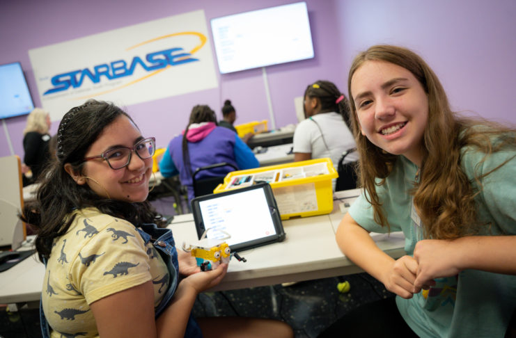 Two middle school girls smile while one holds a robot made out of legos.