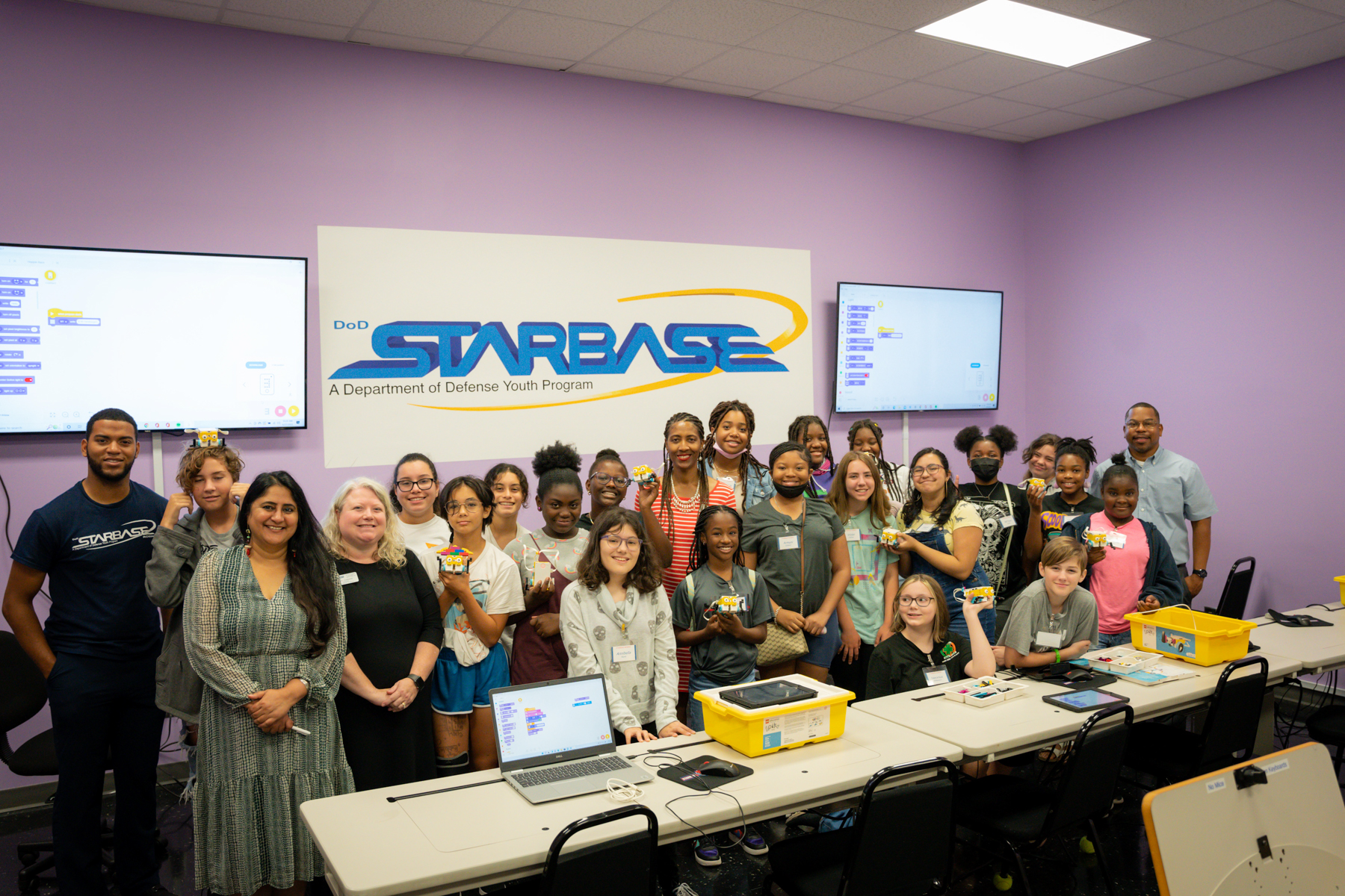 A group of middle school students and a few adults stand in front of a sign that reads: Starbase, a Department of Defense Youth Program