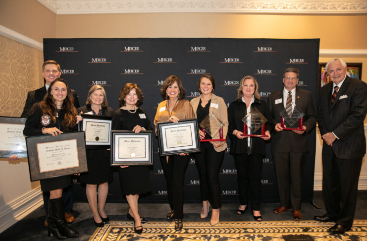 people stand holding awards in front of a mercer backdrop