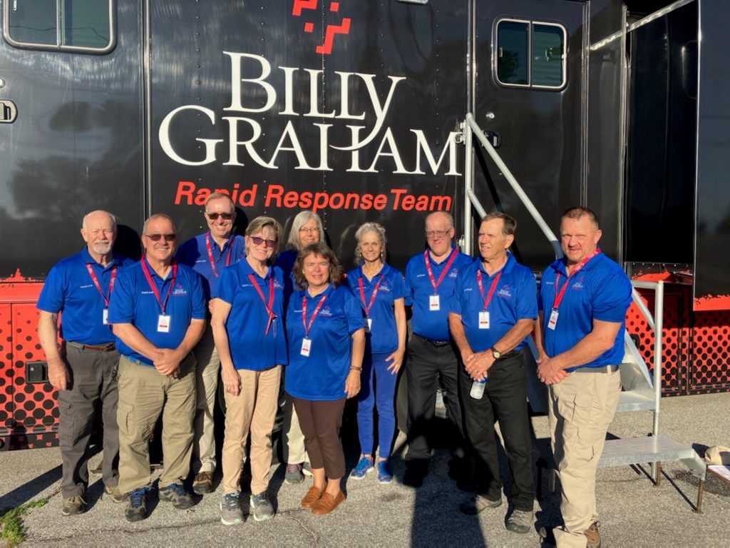 Ten people wearing blue shirts and khaki pants stand in front of a large vehicle that says "Bill Graham Rapid Response Team"
