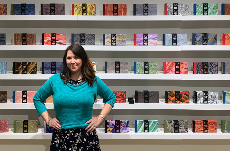 Tennille Shuster stands in front of the pandemic journals she handcrafted.