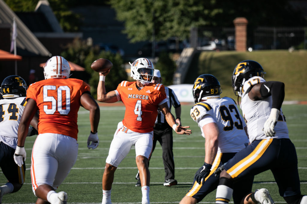 A football player in a orange jersey with the number 4 on it throws the football.