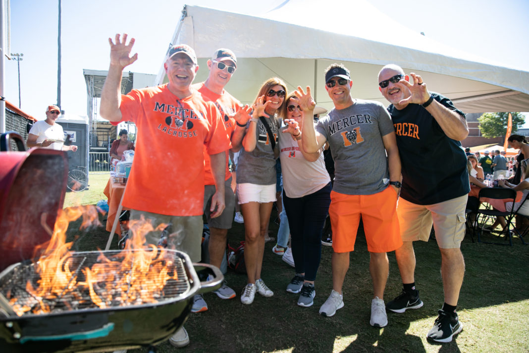 Six people wearing Mercer shirts make their hands into the shape of a claw while standing in front of a grill with flames