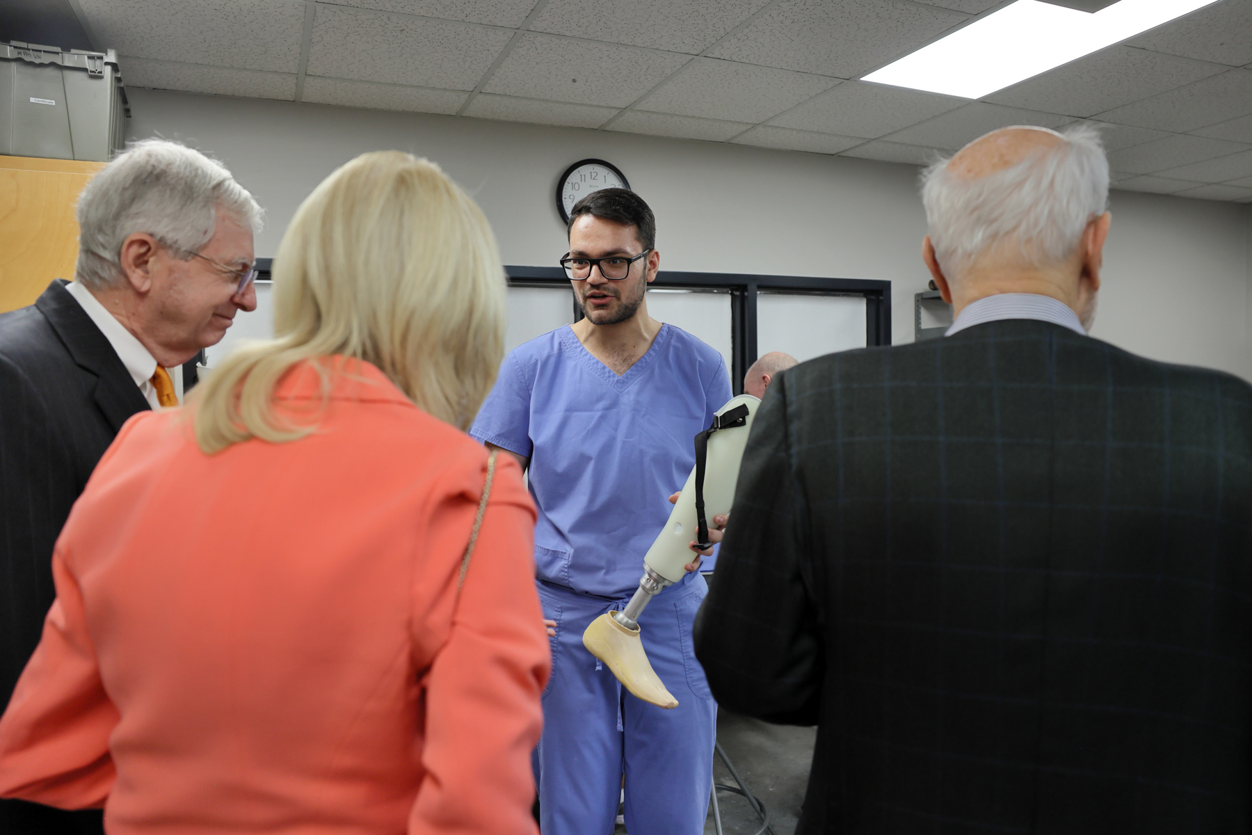 A man in scrubs shows a prosthetic leg to three people wearing suits