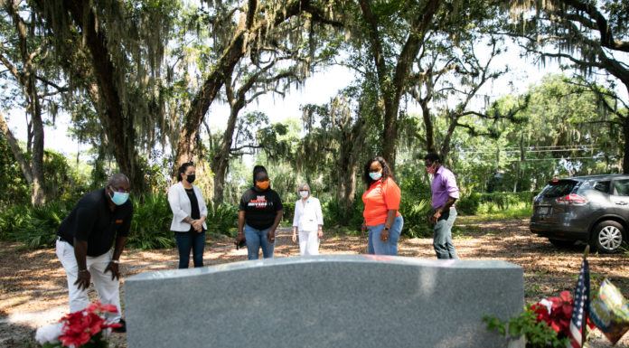 COPA receives Georgia Humanities grant for work to document African American history in Coastal Georgia A group of people standing in front of a gravestone outdoors, wearing masks, surrounded by trees and vehicles.