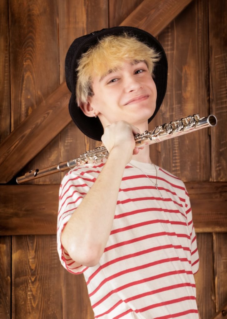 A young person wearing a red and white striped shirt holds a flute on his shoulder