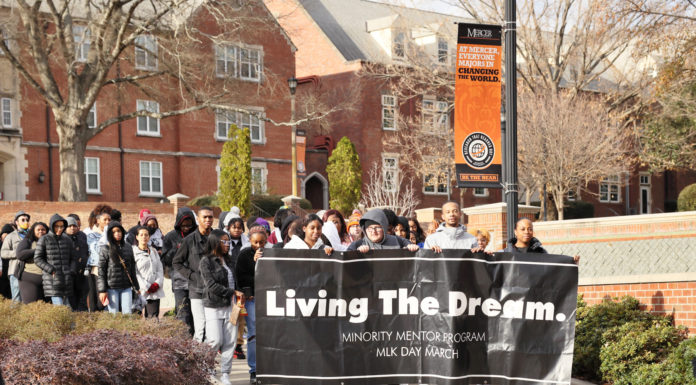 MLK was a voice for those who had none. Will you, too, speak for the voiceless? students march across mercer's campus carrying a banner that says living the dream in white type against a black background