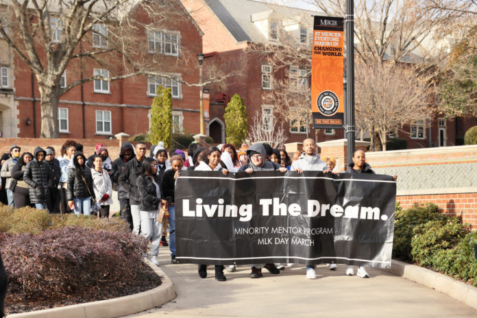 students march across mercer's campus carrying a banner that says living the dream in white type against a black background