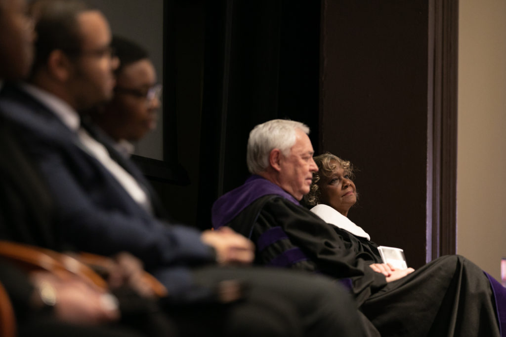 pearlie toliver sits next to president william d. underwood. they are both wearing academic regalia.