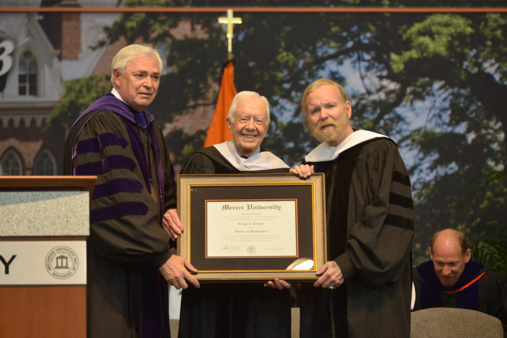 Mercer President William Underwood, Former President Jimmy Carter and Gregg Allman hold Allman's honorary degree on the commencement stage.