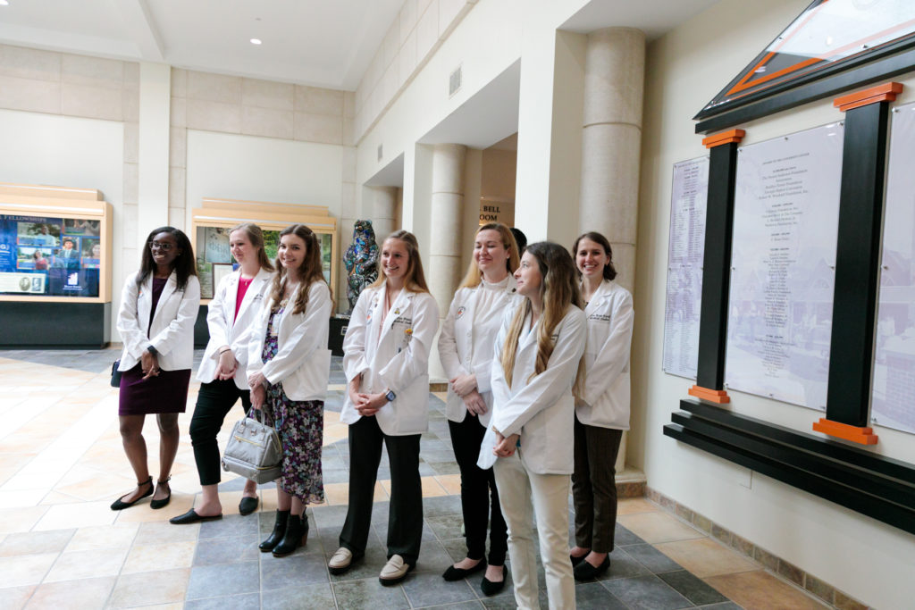 A group of medical school students wearing white coats gather together