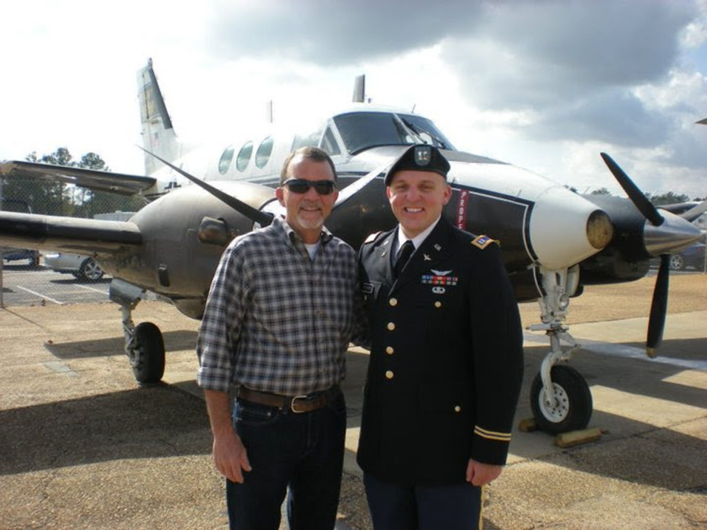 AJ pitchford is wearing a an army officer uniform while standing next to his dad who is wearing civilian clothes. they are both standing in front of an airplane