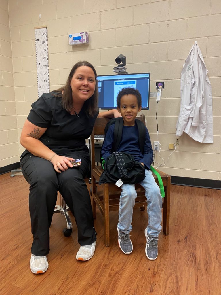 A school nurse sits with a student during a telehealth appointment at school. 