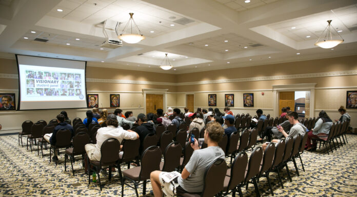 Showcase highlights student ideas for helping their community Audience members are show seated, with a projector in front of them.