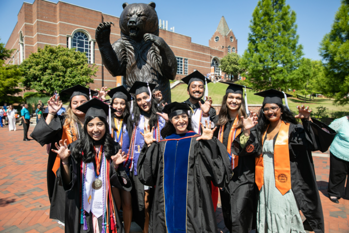 a group of graduates in caps and gowns in front of the bear statue