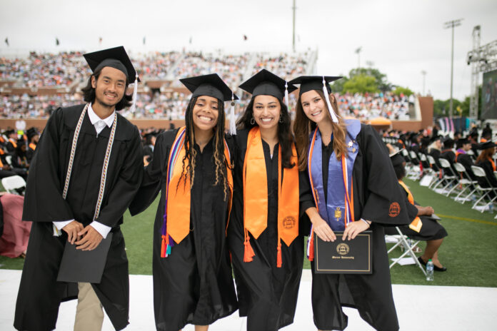 four students pose for a group photo wearing graduation regalia