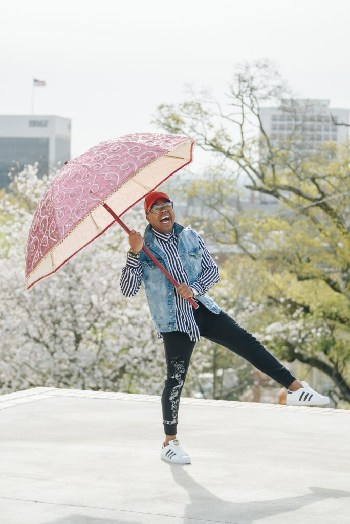 Canaan Marshall lifts one leg in the air while holding an umbrella.