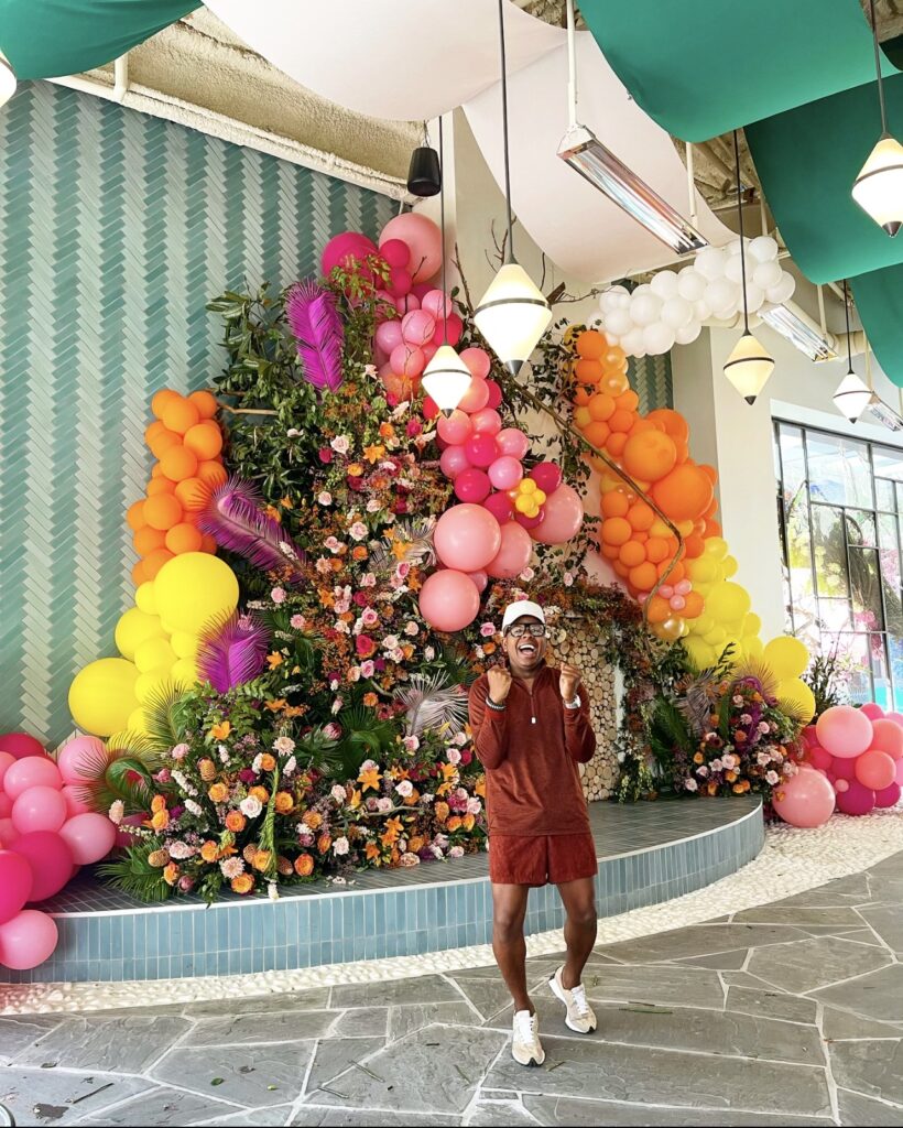 Canaan Marshall stands in front of a vibrant arrangement of flowers and balloons.