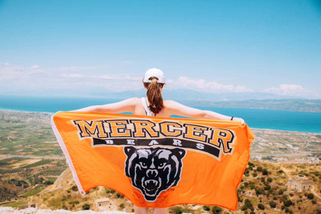 a student holds out a mercer flag overlooking greece