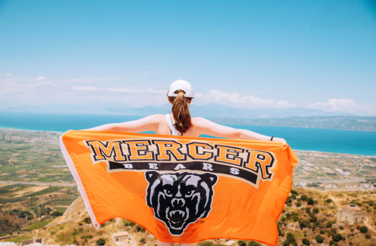a student holds out a mercer flag overlooking greece