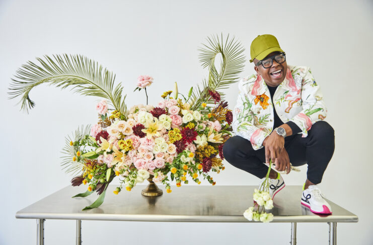 Canaan Marshall crouches on top of a table by a floral arrangement.
