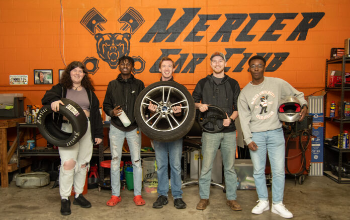 Five students pose for a group photo in the garage, with each holiday a piece of automotive equipment.
