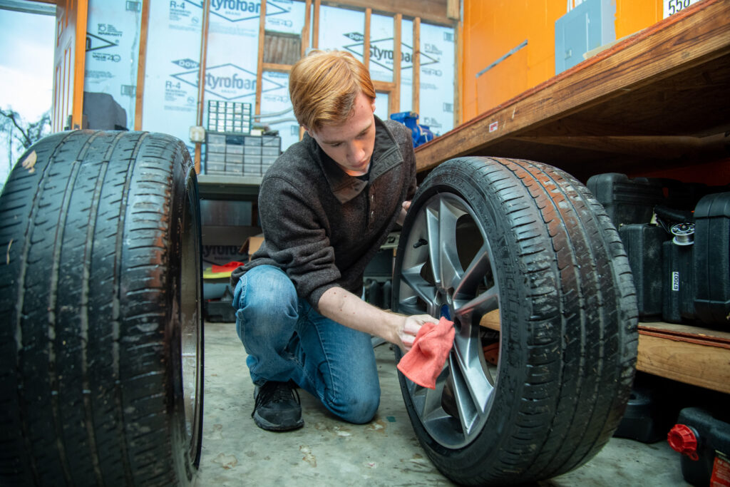 A student holds a tire and cleans its wheel.