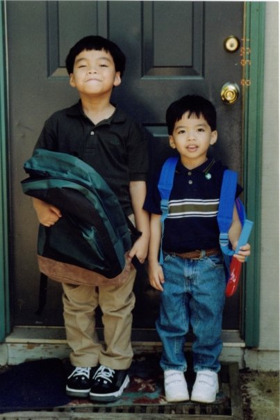 two kids stand in front of a door with backpacks