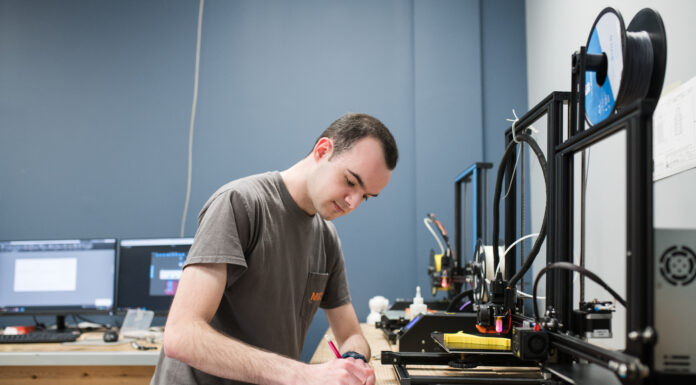 Students design instructional materials to streamline robotics lab training A student writes on paper in front of machines in the lab.