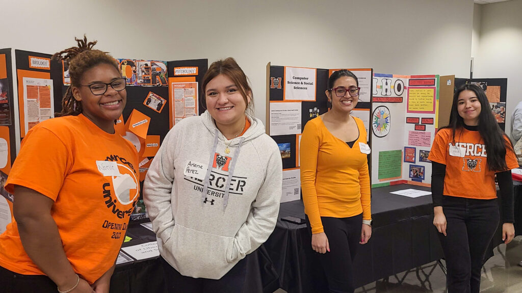 Four students wearing Mercer clothing stand beside the posters they made.
