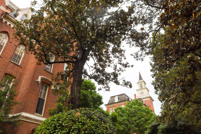 The administration building is seen up close, with the top of Willet Hall seen in background through the trees.