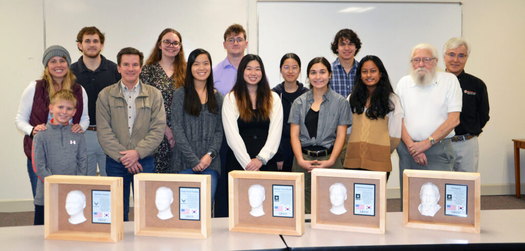 A group of people stands behind a table with five 3D plaques.