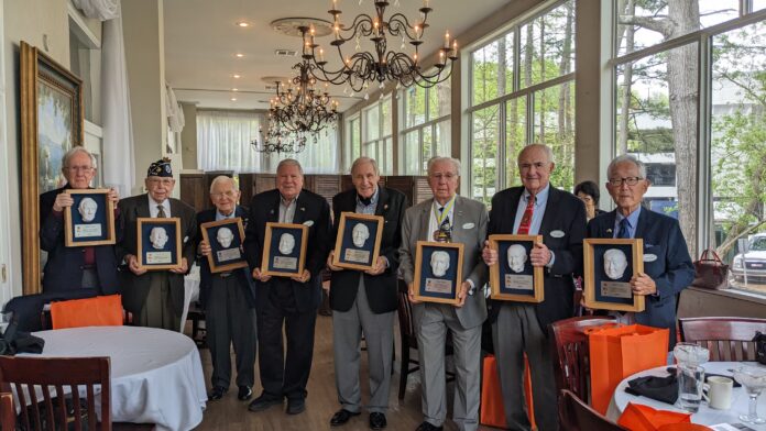 Eight veterans stand holding their plaques.