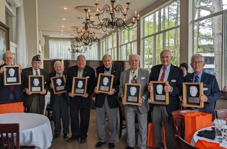 Eight veterans stand holding their plaques.
