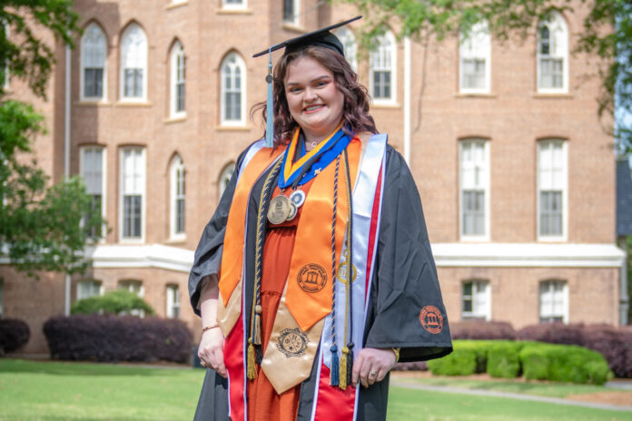 lara edgeman wears graduation gear in front of the administration building