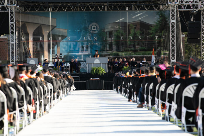 student speaks at a podium in front of graduates