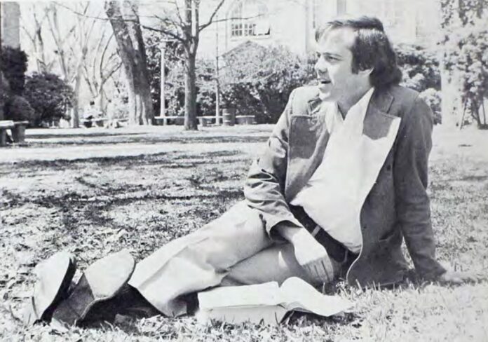 Dr. Mike Cass sitting in the grass on campus with a book.