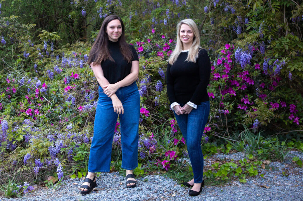 two women stand in front of a flowering bush