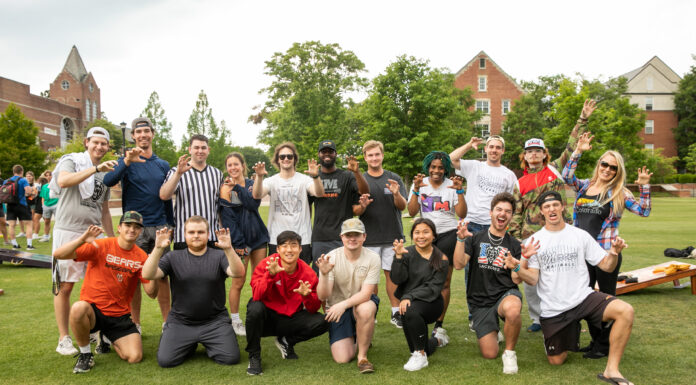 New course gives students real-world sports marketing experience A group of students and faculty huddle together and make the bear claw motion with their hands.