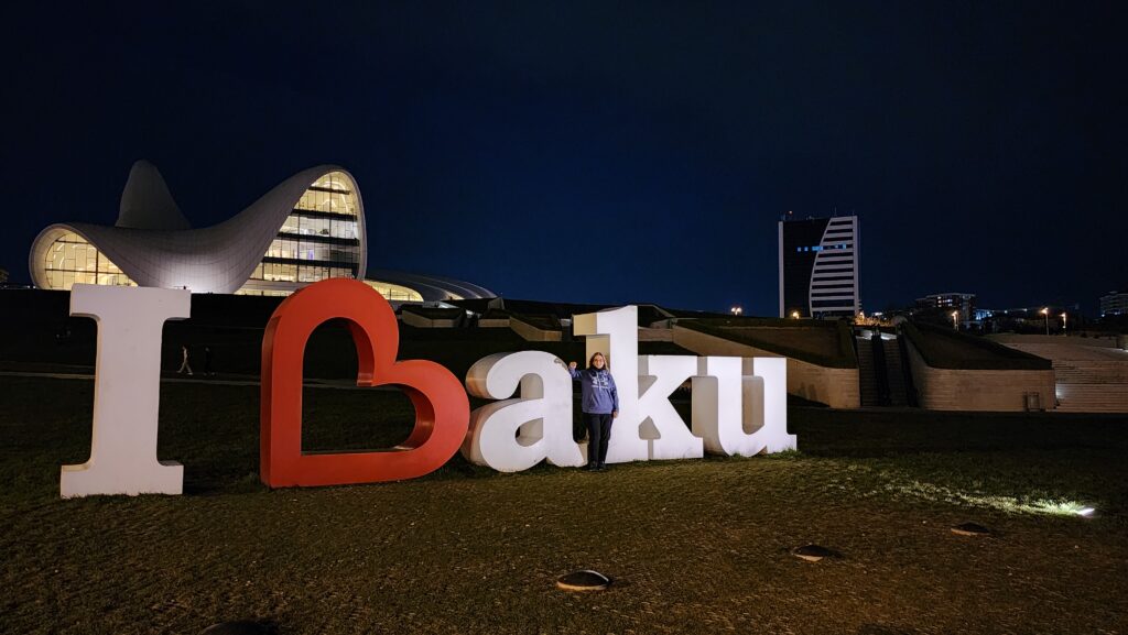 Dr. Jacqueline Stephen stands in front of a large letters that say "I love Baku," with tall buildings in the background.