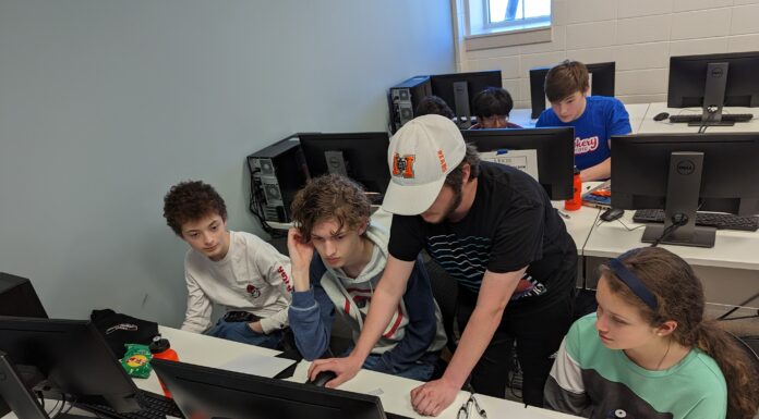 Class of 2023 graduates plan Mercer’s first high school coding contest A Mercer student leans over a desk to help a team of students at their computer.