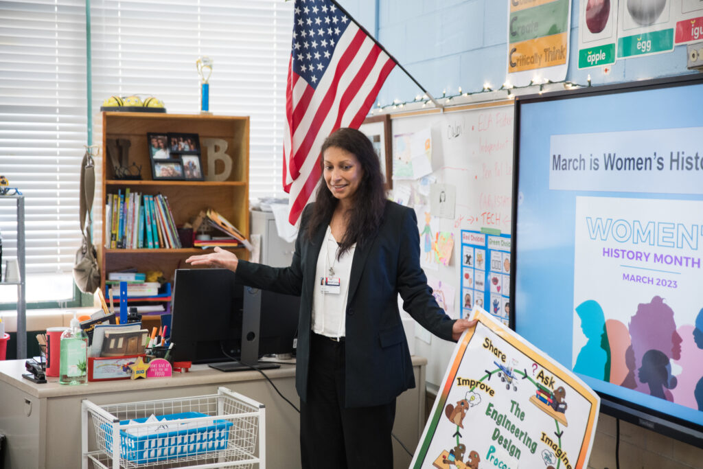 Veena Black holds a poster and talks while teaching a lesson in her classroom.
