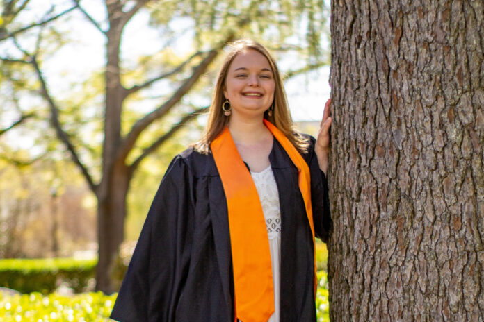 Gwenevere Wrye wears a black graduation gown and orange stoll