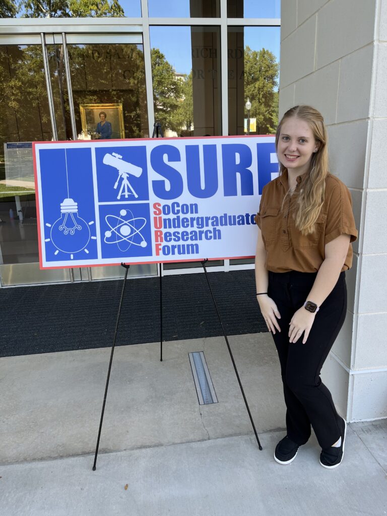 Bryana Whitaker stands in front of a sign for the conference.