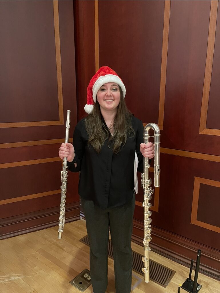 Dakota Ellis wears a Santa hat and holds a flute in one hand and alto flute in the other.