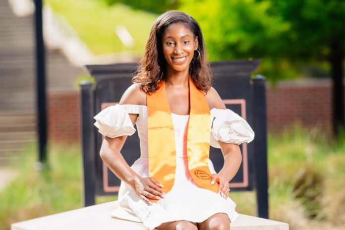 Emily Ogbodo wears a white dress and orange stoll