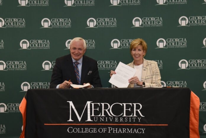 GCSU president holds up a piece of paper. Mercer president sits on her left.
